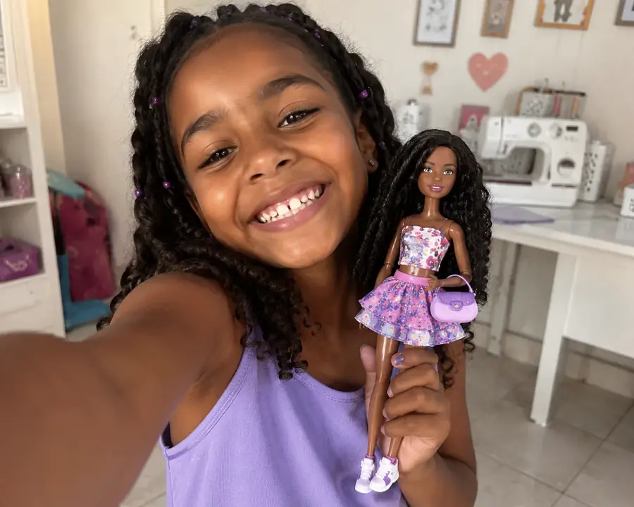 Ni&ntilde;a sonriendo en un taller con una fashion doll vestida con un look artesanal